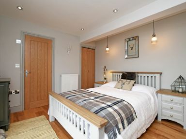 A bedroom with a bed a checkered blanket pillows two wooden doors bedside tables and hanging lights at The Hemmel Beadnell