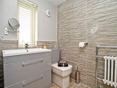 A bathroom with a sink and cabinet window toilet toilet brush and tiled walls at The Hemmel Beadnell