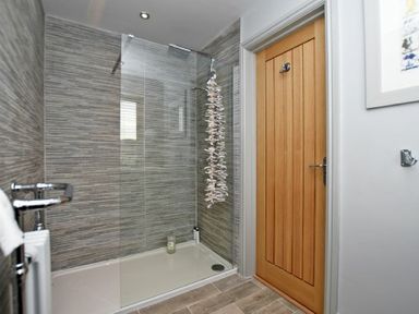 A bathroom with a walk in shower glass door wooden door and wall hooks at The Hemmel Beadnell