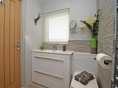A bathroom with a white cabinet sink a window with blinds and a closed wooden door at The Hemmel in Beadnell