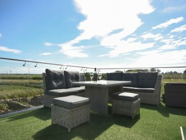An outdoor seating area with cushioned wicker sofas stools and a table with wine glasses on artificial grass at The Hemmel Beadnell