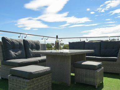 Outdoor seating area with wicker furniture and cushioned sofas with a table holding a bottle and glasses at The Hemmel (Beadnell) in Beadnell