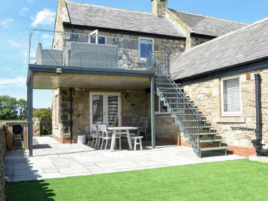 An outdoor patio area with a table and chairs under a balcony with stairs leading up to the balcony at The Hemmel Beadnell