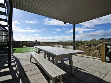 An outdoor covered patio with a dining table bench and chairs on a stone floor at The Hemmel (Beadnell) in Beadnell