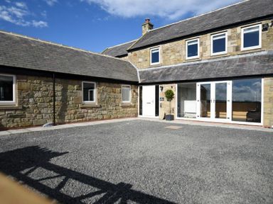 An exterior view of a stone building with multiple windows and glass doors surrounding a gravel courtyard at The Hemmel Beadnell