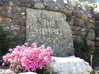 A stone sign engraved with the words The Hemmel surrounded by pink flowers and a stone wall in the background at The Hemmel in Beadnell