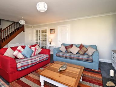 A living room with two sofas a wooden coffee table and a staircase at Armstrong Cottages No22 in Bamburgh