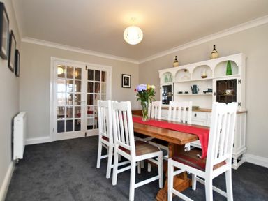 A dining room with a wooden table and white chairs with a red runner and flowers at Armstrong Cottages No22 in Bamburgh