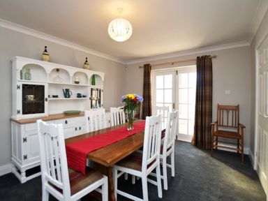 A dining room with a wooden table and white chairs and a white cabinet with dishes at Armstrong Cottages No22 Bamburgh