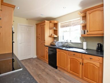 A kitchen with wooden cabinets black appliances and a window at Armstrong Cottages No22 Bamburgh