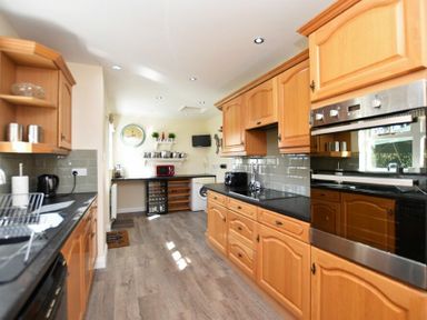 A kitchen with wooden cabinets black countertops a wall clock and appliances at Armstrong Cottages No22 Bamburgh