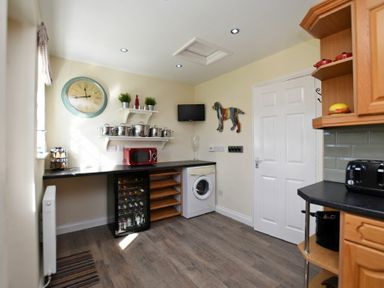 A kitchen with a washing machine wine cooler microwave and shelves with pots and plants at Armstrong Cottages No22 in Bamburgh