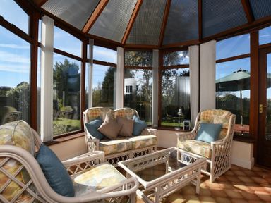 A sunroom with wicker chairs and a glass coffee table surrounded by windows at Armstrong Cottages No22 in Bamburgh