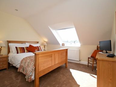 A bedroom with a wooden bed a bedside table with lamps a desk with a computer and a chair under a skylight window at Armstrong Cottages No22 in Bamburgh