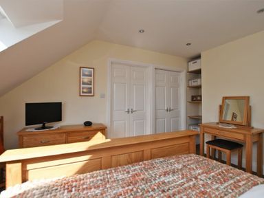 A bedroom with wooden furniture including a bed dresser and vanity table with a mirror at Armstrong Cottages No22 in Bamburgh