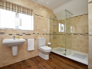 A bathroom with a sink toilet glass shower and wooden floor at Armstrong Cottages No22 in Bamburgh