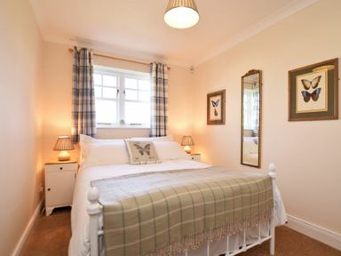 A bedroom with a double bed two bedside tables with lamps a window with curtains and butterfly framed pictures at Armstrong Cottages No22 in Bamburgh
