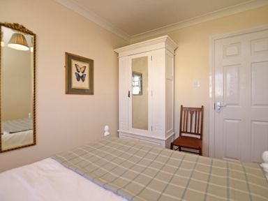 A bedroom with a bed a white wardrobe a wooden chair a framed butterfly picture and a wall mirror at Armstrong Cottages No22 in Bamburgh