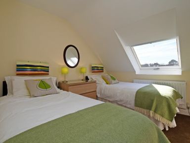 A bedroom with two single beds, a wooden dresser, two lamps, a round mirror, and a skylight window at Armstrong Cottages No22 in Bamburgh