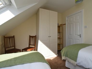 A bedroom with two single beds with green blankets two wooden chairs a white wardrobe and a wooden shelf at Armstrong Cottages No22 in Bamburgh