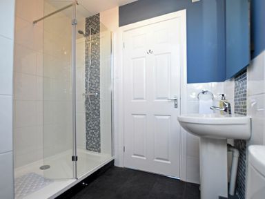 A bathroom with a walk-in glass shower, white door, sink with faucet, blue wall cabinet and tiled wall at Armstrong Cottages No22 Bamburgh