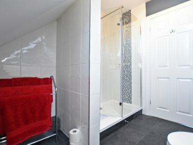 A bathroom with a glass shower enclosure red towels on a rack and a white door at Armstrong Cottages No22 Bamburgh