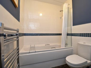 A bathroom with a bathtub shower combination a white toilet and a heated towel rail at Armstrong Cottages No22 in Bamburgh