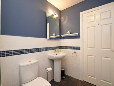 A bathroom with a toilet a pedestal sink a mirror a door and blue and white tiled walls at Armstrong Cottages No22 in Bamburgh