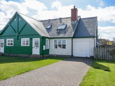 A semi detached house with a green and white exterior and a driveway at Armstrong Cottages No22 in Bamburgh