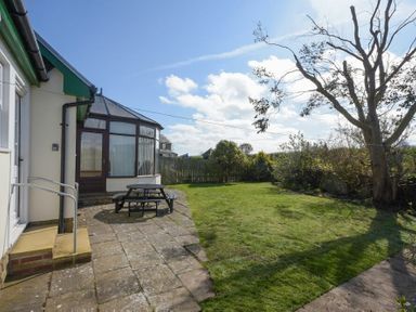 A garden with a lawn and a patio area with a picnic table outside a house at Armstrong Cottages No22 in Bamburgh