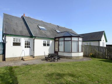 A house with a sloped roof and skylights next to a small patio with a picnic table and a grassy yard at Armstrong Cottages No22 in Bamburgh