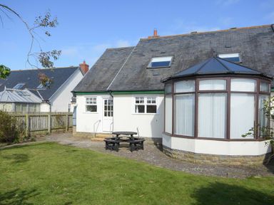 A backyard with a green lawn a picnic table and a house with a bay window at Armstrong Cottages No22 in Bamburgh