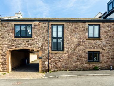 A stone building with black framed windows and an archway driveway at Harbour Lights House in Seahouses