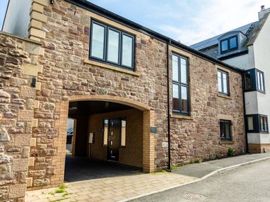 The exterior of a stone building with several black-framed windows and an arched entrance at Harbour Lights House in Seahouses