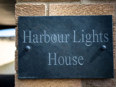 A sign with the text Harbour Lights House mounted on a stone wall at Harbour Lights House in Seahouses