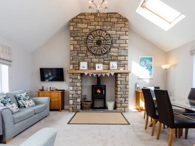 A living room with a stone fireplace a clock above and a sofa and dining table at Harbour Lights House in Seahouses