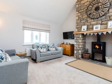 A living room with sofas a stone fireplace with a wall clock and a television at Harbour Lights House in Seahouses