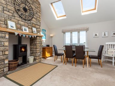 A dining room with a glass table and four chairs near a stone fireplace with a clock above at Harbour Lights House in Seahouses
