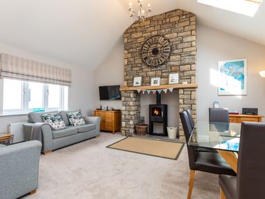A living room with a stone fireplace and a wall clock above it at Harbour Lights House in Seahouses