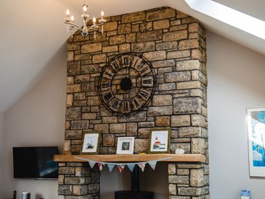 A stone fireplace with a large clock above and framed pictures on the mantel at Harbour Lights House in Seahouses