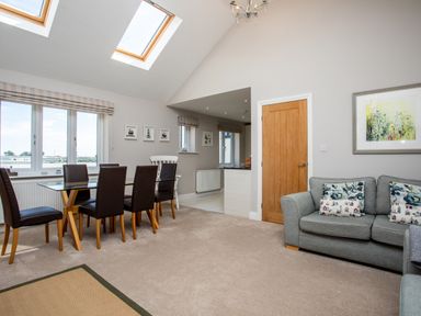 An open living and dining area with a glass dining table and chairs a grey sofa and a wooden door at Harbour Lights House in Seahouses