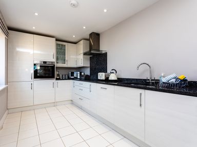 A kitchen with white cabinets black countertop oven microwave and sink at Harbour Lights House in Seahouses
