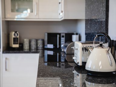 A kitchen counter with a kettle toaster microwave coffee machine and ceramic canisters at Harbour Lights House in Seahouses