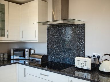 A kitchen counter with a microwave two canisters a bread bin a stovetop a toaster and a kettle at Harbour Lights House in Seahouses