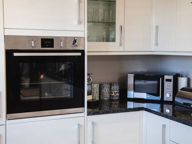 A kitchen corner with an oven microwave canisters and glass front cabinets at Harbour Lights House in Seahouses