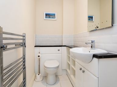 A bathroom with a toilet a sink a towel rack and a small painting on the wall at Harbour Lights House in Seahouses