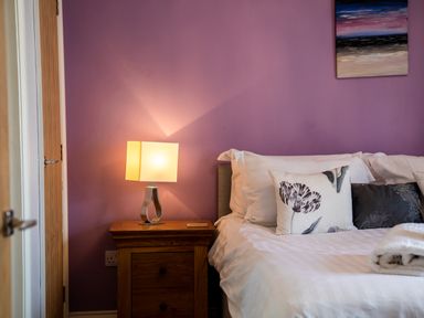 A bedside table with a lamp next to a bed with pillows and a folded towel at Harbour Lights House in Seahouses