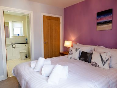 A bedroom with a bed and pillows towels on the bed a side table with a lamp and an adjoining bathroom at Harbour Lights House in Seahouses