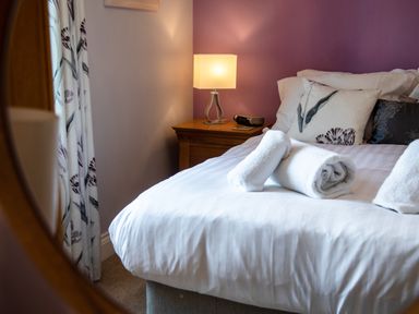 A bedroom with a bed featuring white rolled towels a bedside table with a lamp and floral curtains at Harbour Lights House in Seahouses