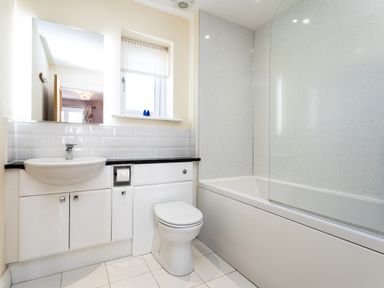 A bathroom with a sink cabinet a toilet and a bathtub with shower screen at Harbour Lights House in Seahouses